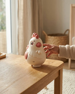 White and pink egg-laying chicken toy on wooden table, hand holding