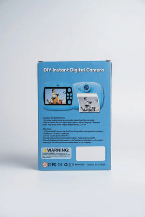 Blue instant print camera with rear display, paper rolls, wrist strap, USB cable and instruction booklet