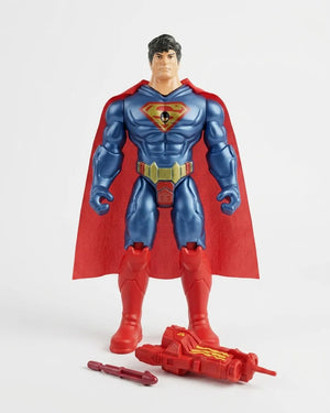 Superman action figure with a red cape, blue suit, and gold belt, standing on a light gray background with a red weapon accessory in front.