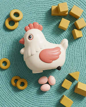 White and pink egg-laying chicken toy on teal mat with wooden blocks