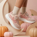 Pink girls' sneakers with lace-up front, strap and white chunky sole worn on foot