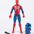 Spider-Man action figure in red and blue with a large white spider emblem on the chest, standing on a white background with a small black accessory and a blue component beside it.
