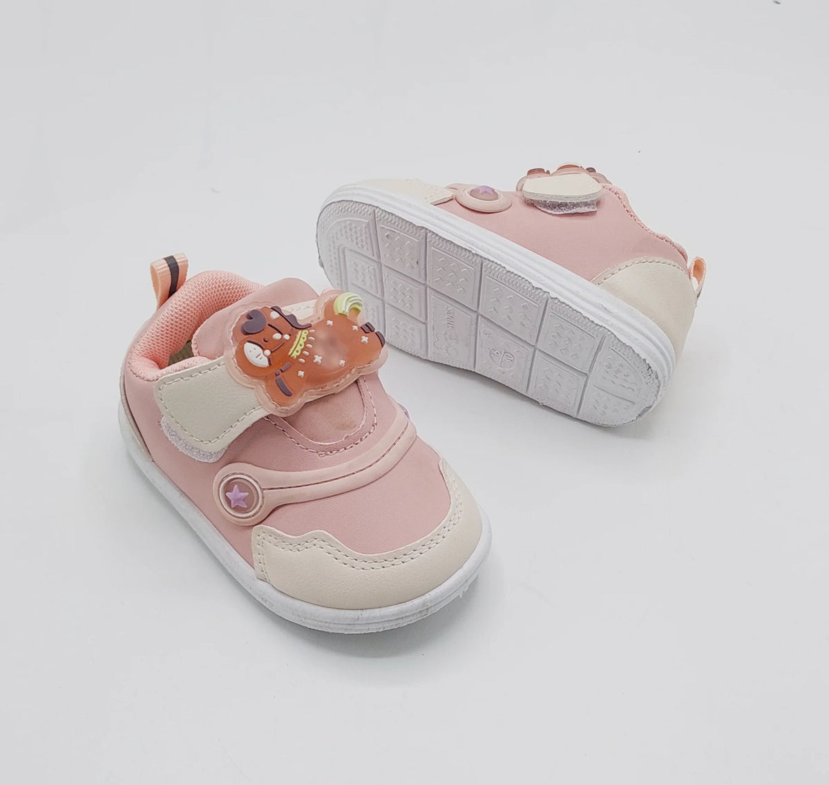 Light pink kids' sneakers showing textured white outsole with circular bear logos